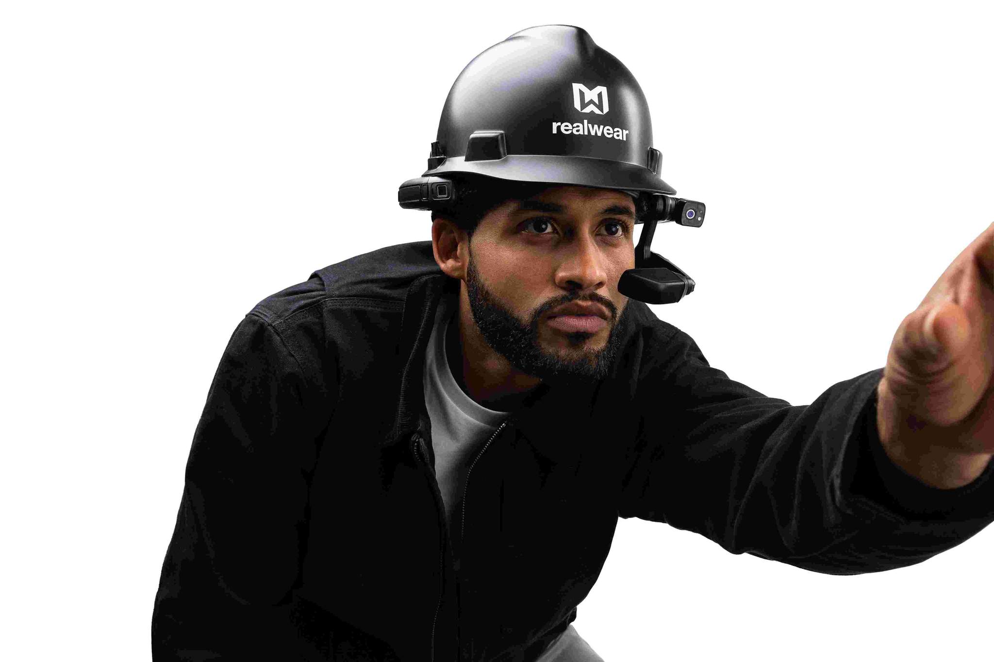 A man wearing a black RealWear Navigator™ 500 Rugged Handsfree Tablet hard hat with a noise-canceling headset, reaching forward with his right hand. White background.
