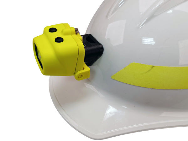 A white safety helmet with a Nightstick XPP-5454GC Zone 0 IS Dual-Light Headlamp in yellow, attached by a hard hat clip to the front, features black buttons and a reflective yellow strip on the helmet.