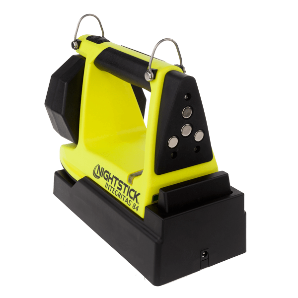 A yellow and black Nightstick XPR-5584GMX INTEGRITAS™ Intrinsically Safe Rechargeable Lantern with a magnetic base is placed on its charging station against a white background.