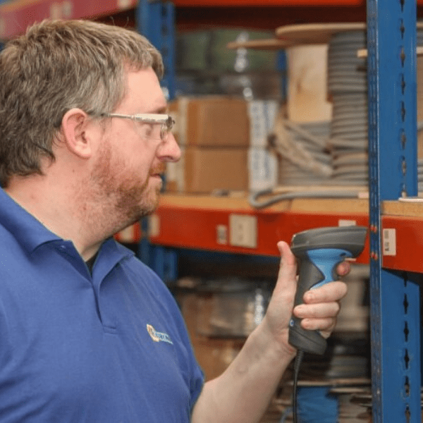 A man in a blue shirt scans a barcode on a warehouse shelf using the Extronics iSCAN101 Series Zone 1 Barcode Laser Scanner.