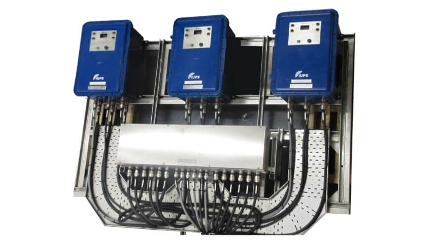 Three blue Extronics iUPS101 Zone 1 and 2 Uninterruptible Power Supply units, ATEX certified, are mounted above a metallic box, with multiple black cables neatly connected and organized underneath.