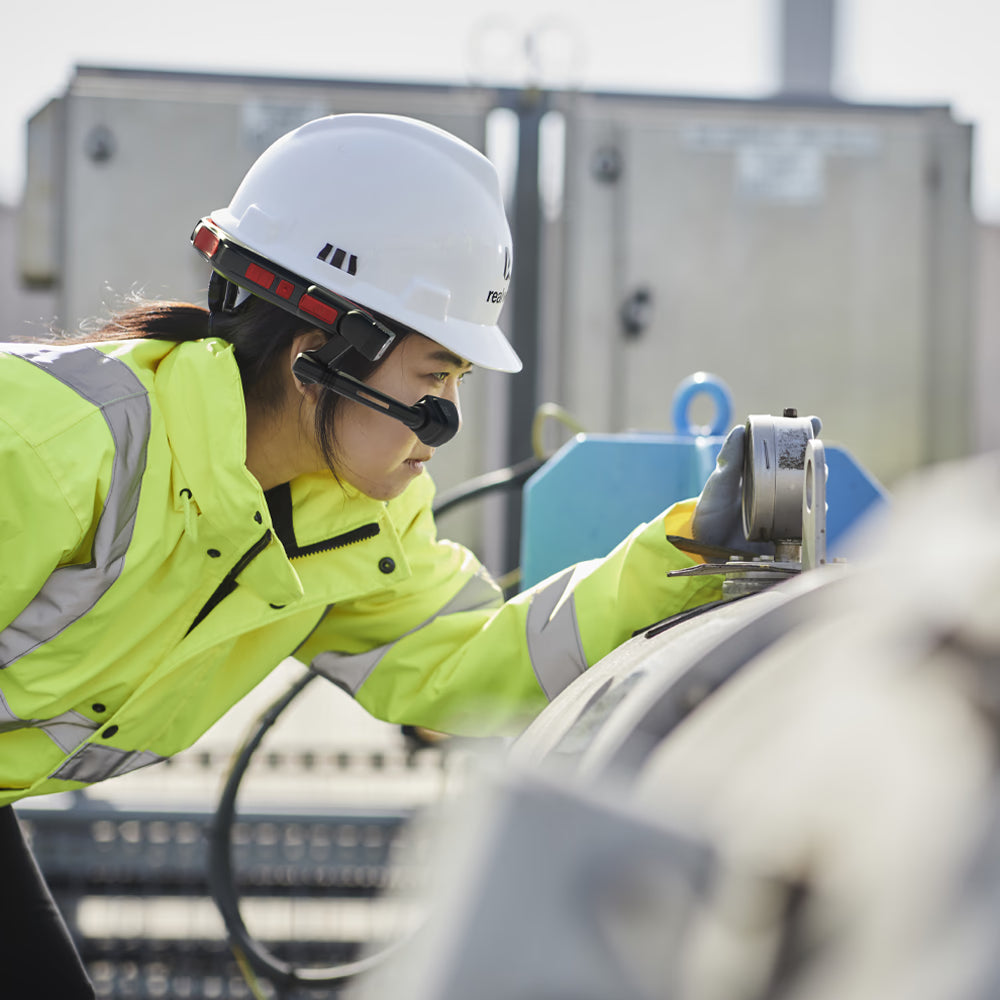 A worker in a high-visibility jacket and hard hat uses the RealWear Navigator Z1 with Thermal Camera to inspect industrial equipment outdoors in an ATEX Zone 1 area for enhanced safety.