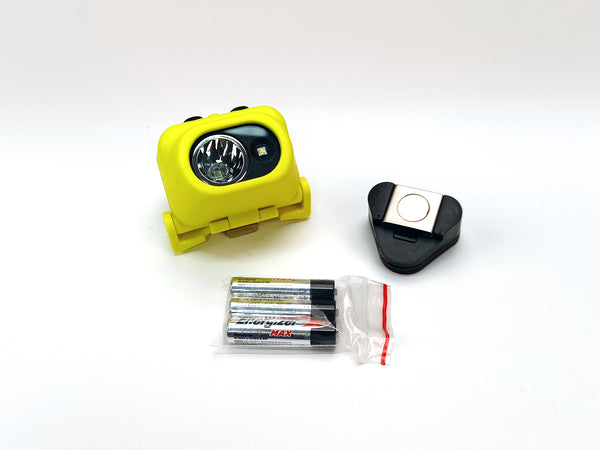 A Nightstick XPP-5454GC [Zone 0] IS Dual-Light Headlamp in yellow, with a black hard hat clip and three AA Energizer Max batteries in a plastic bag, is arranged on a white background.