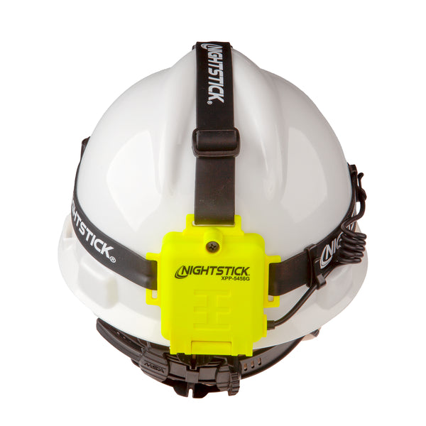 A white hard hat with a black strap features the Nightstick XPP-5456G [Zone 0] IS Permissible Dual-Light Headlamp in bright yellow, offering hands-free, advanced illumination. The Nightstick logo appears on both the headlamp and strap.